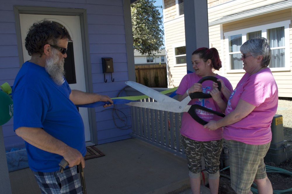 People cutting a ribbon with giant scissors at a house ceremony