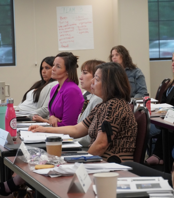 People attentively listening during a classroom training session with notes and coffee cups on desks
